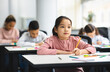 © Prostock-studio - Elementary School Class. Portrait of Cute Little Asian Girl Smiling, Taking Notes And Writing in Exercise Notebook. Junior Classroom with Diverse Group of Children Learning New Stuff