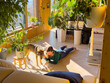 © helivideo - Woman lies on the floor and shows her curious dog a page in book she is reading. Young dog owner and her pet relax in living room filled with lush plants and warm sunlight streaming in through windows
