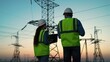 © Victoriia - Business people, power construction. Two energy engineers work with computer tablet outdoors. Engineers in helmet, on field with electric towers, teamwork. Electrical with high voltage pylon, sunset.