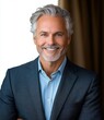 © Donna - Confident mature man with gray hair and beard smiling warmly in smart casual business attire against a blurred neutral background