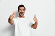 © SHOTPRIME STUDIO - Full body smiling joyful young man gives thumbs up, wear casual white t-shirt, look at camera, isolated on clean solid light background studio portrait. People happiness concept