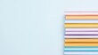 © CoreVisuals - A neatly stacked pile of colorful books is arranged against a light blue background, creating a simple and modern composition.
