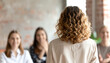 © justholla - A woman with curly hair stands facing an audience, engaged in a presentation, while the audience responds positively