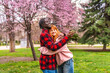 © unai - Interracial couple embracing and taking selfie in blooming park