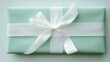 © Vitalii - Close-up of a gift box wrapped in light green paper. the box is square in shape and has a white ribbon tied in a bow on top. the ribbon is neatly tied with a thin white ribbon.