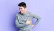 © Atikoh - Young adult man experiencing chest pain or heart attack with hand on chest and back, expressing pain and discomfort against purple backdrop