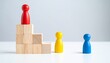 © photostockatinat - Three wooden figures stand on a staircase made of wooden blocks. The red figure is at the top, while the yellow and blue figures are at the bottom.