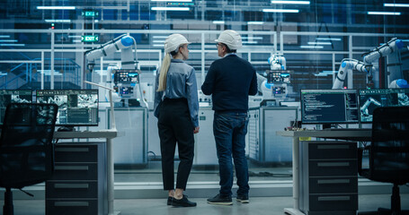 Fototapete - System Administrator and Technician Working at a Manufacturing Plant. Male Specialist Programming the Work of the Robotic Arms, Explaining Production on the Assembly Conveyor to a Female Colleague