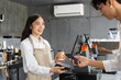 © itchaznong - Customer Service and Payment Process. A cheerful barista assisting a customer with a mobile payment at a cafe.