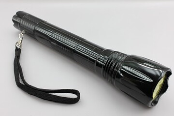 Poster - Black flashlight with textured grip and lanyard intended for outdoor and emergency use in low-light conditions