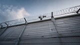 cold grey prison wall with barbed wire fence surrounding a maximum security area barbed wire fences surveillance cameras