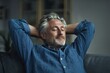 © ngalong project - Man with gray hair relaxes on a couch with hands behind head.