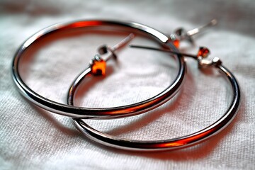 Poster - Silver hoop earrings resting on a textured fabric surface with soft lighting in a serene indoor setting
