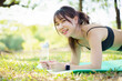 © DG PhotoStock - Asian woman training core muscles outdoors with plank and side plank poses under a tree in the park.