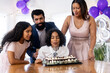 © Wavebreak Media - Diverse family celebrating birthday with cake and balloons, child blowing out candles, at home