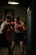 © WoodHunt - A focused boxer wearing red gloves is punching a heavy bag in a dimly lit gym. The background shows old boxing posters and a worn-out wooden floor