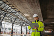 © Halfpoint - Female engineer checking building documentation on clipboard at construction site.