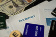 © noktunstudio - Top view of tax paperwork with 'TAX REPORT' headline, American dollar bills, and credit cards scattered on the desk. The scene portrays a realistic representation of annual tax return preparation
