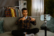 © kinomaster - Young african american child boy spending time at home, kid blogger sits on sofa records video on smartphone, talking at camera and gives review.