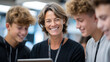 © Maksym - Group of students gathered around smiling teacher holding tablet, engaged in collaborative learning activity in a well-lit room