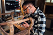 © Zoran Zeremski - Carpenter standing in his workshop restoring old piece of furniture with mini grinder.