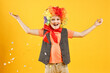 © New Africa - Happy little boy dressed like clown and flying confetti on orange background. Surprise party