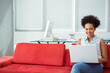 © WavebreakMediaMicro - Smiling woman typing on red sofa in modern office lounge, with silver laptop, copy space