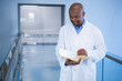 © WavebreakMediaMicro - African American male doctor reviewing yellow folder in hospital corridor, copy space
