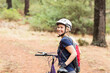 © WavebreakMediaMicro - Holding purple bicycle woman cyclist standing on forest trail with red backpack, copy space