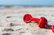 © Emanuel - Red old-fashioned telephone receiver on sand at beach