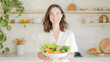 © Jirawatfoto - smiling woman holding bowl of fresh vegetables, including lettuce, broccoli, and carrots, bright kitchen setting, promoting health and detox