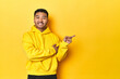 © Asier - Bold Asian man in yellow hoodie on yellow studio smiling cheerfully pointing with forefinger away.