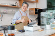 © Rakchanok - Senior entrepreneur cafe owner barista hold POS machine to customer, Asian female in apron welcome warmly in counter, croissants and glassware background, retired elderly woman start small business