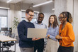 © anatoliycherkas - Professional team collaborating around laptop, representing workplace diversity and modern corporate interaction