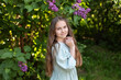 © stock_studio - Closeup Portrait of a pretty young little girl with long hair and in dress is standing in a lilac spring garden. Gardening, florist, flower girl. Allergy free. A child girl walks in a flowered park.