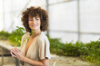 © DMegias - Smiling female gardener holding fresh seedling inside indoor greenhouse