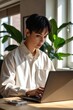 © kineter_ai - Focused East Asian Non-Binary Male Young Adult Using Laptop in Bright Office with Large Leafy Plants