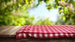 © CreativeCreations - Empty wooden desk table with red checkered tablecloth over abstract bright light green spring or summer background, template for your food and product display montage