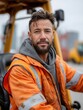© Mykhailo - Male construction worker wearing safety jacket and hood sitting outdoors near construction vehicles on cloudy day
