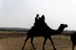 © explorewithinfo - tourist enjoying camel ride in desert with bright sky at day backlit shot
