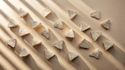 Poster - Triangular stone objects arranged in a repeating pattern, illuminated by soft sunlight casting shadows on a beige surface