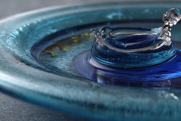 Poster - Droplet creating ripple effect on blue glass surface with artistic reflections and textures during bright daylight