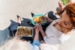 © Dani D.G - Businesswomen sharing lunch break on urban pavement, eating healthy meals from containers and laughing together under bright sunlight