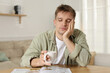 © New Africa - Suffering from hangover. Unhappy young man with cup of coffee sitting at wooden table indoors