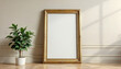 © pixdots - An empty golden frame beside a potted plant in a room with natural light, creating a sense of anticipation and display potential.