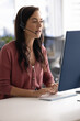 © fizkes - Call center. Vertical photo busy millennial female customer support manager in headset with microphone sitting before desktop computer talking to client via video call giving professional consultation