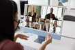 © fizkes - Conference call. Over shoulder view young businesswoman in earphones with mic talk to diverse partners group on remote business event before pc screen leading workshop training in corporate video chat