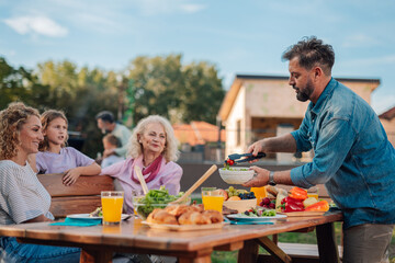 family enjoying backyard barbecue, serving fresh salad at the table