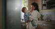 © Marco - Mother smiling at baby in kitchen, casual parenting and bonding moment during warm family morning routine, home life with nurturing and love