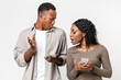 © Prostock-studio - African american woman with smartphone spying on her boyfriend chatting on mobile phone, grey studio background. Black couple using phones, woman does not trust her man, technologies and relationships